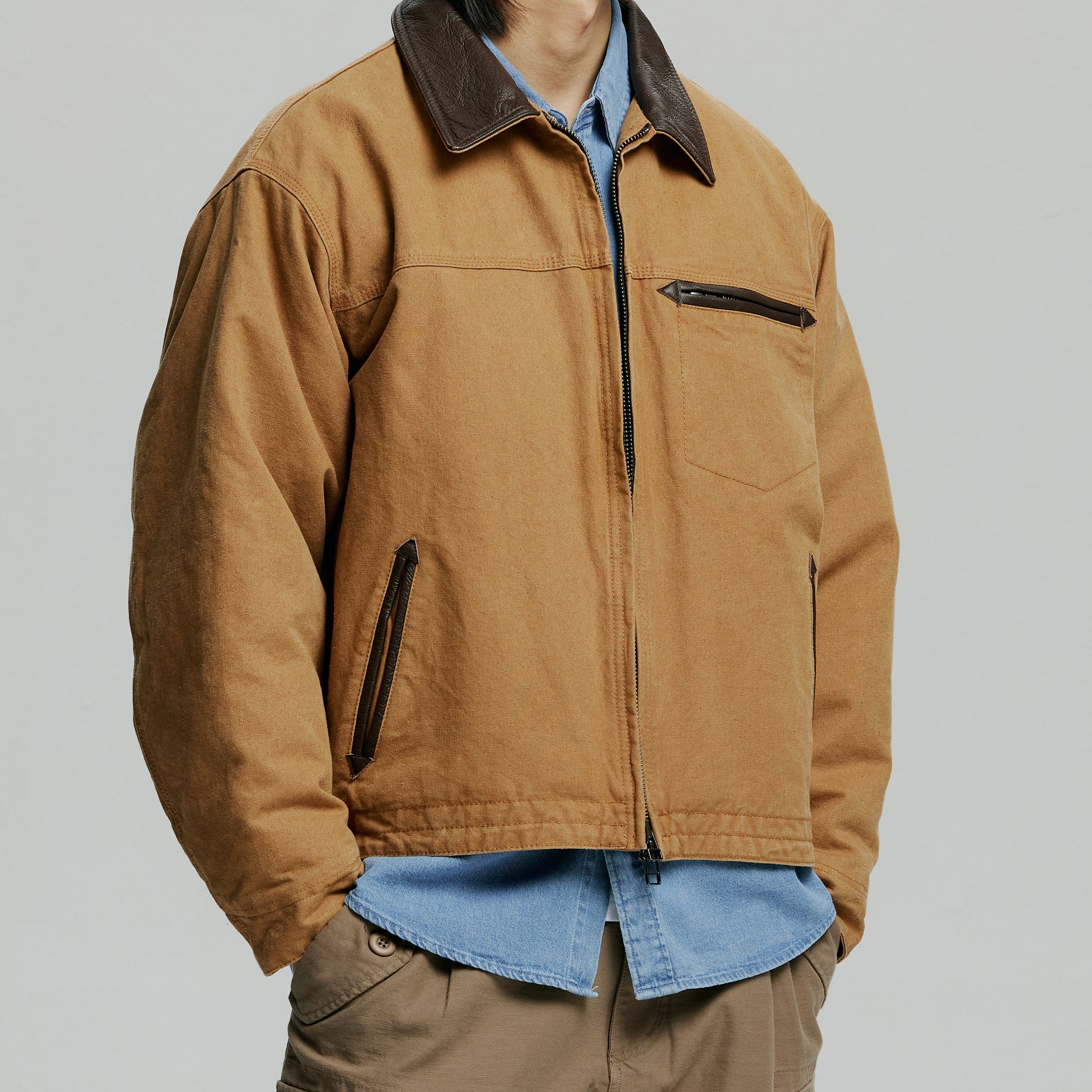 Person wearing a brown jacket over a blue shirt on a plain background
